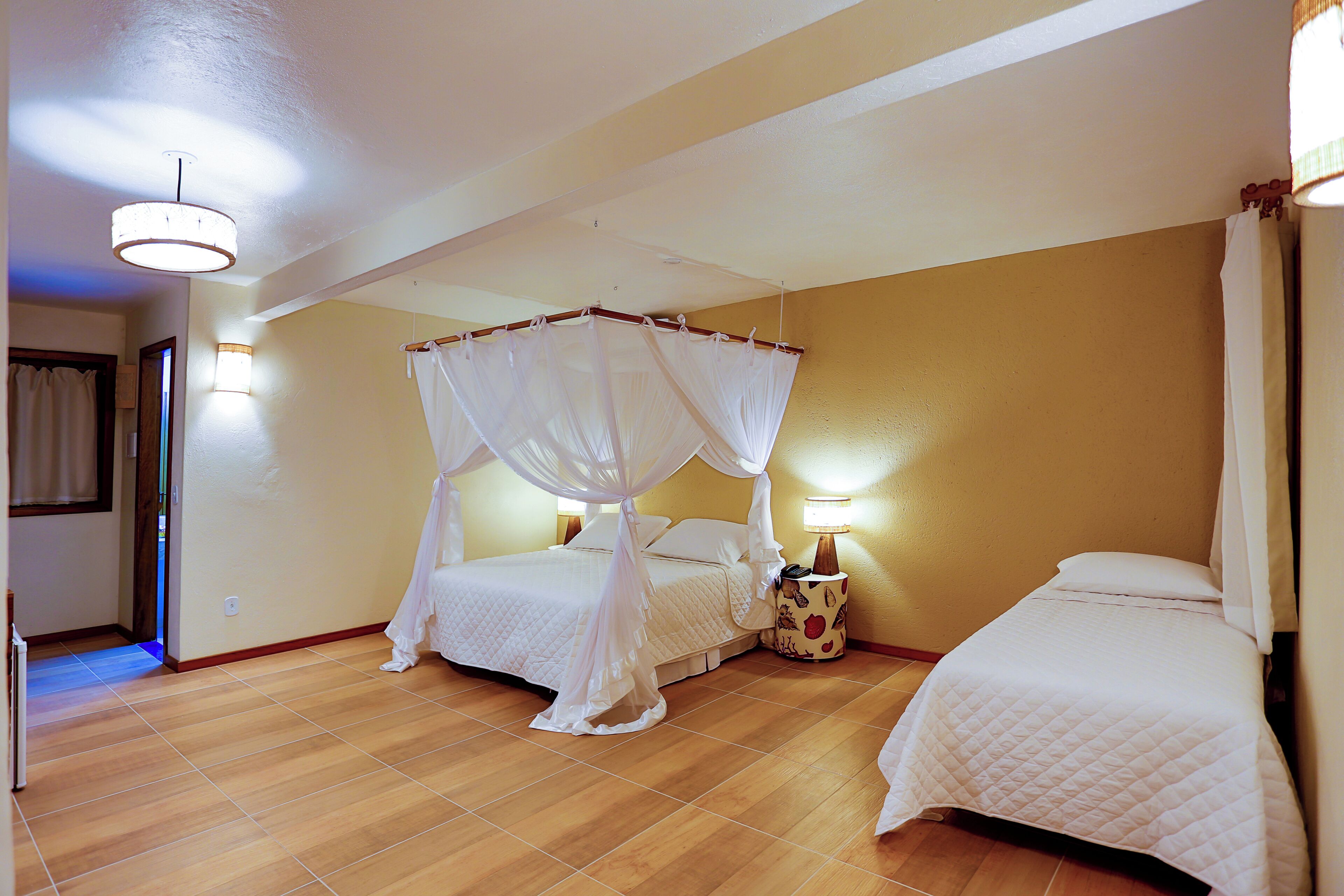 A bedroom with a four-poster bed, a bedside table with a lamp, and a separate bed.