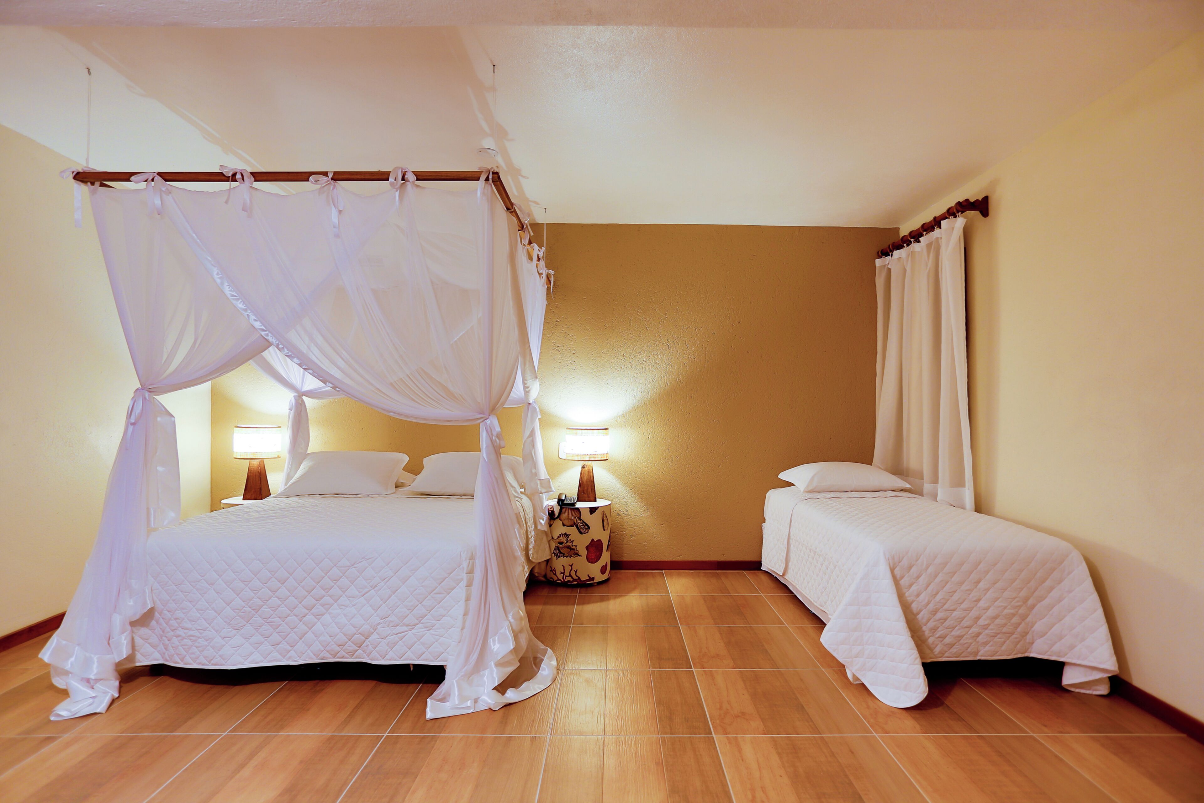 A bedroom with a four-poster bed, a single bed, and a nightstand with a lamp.