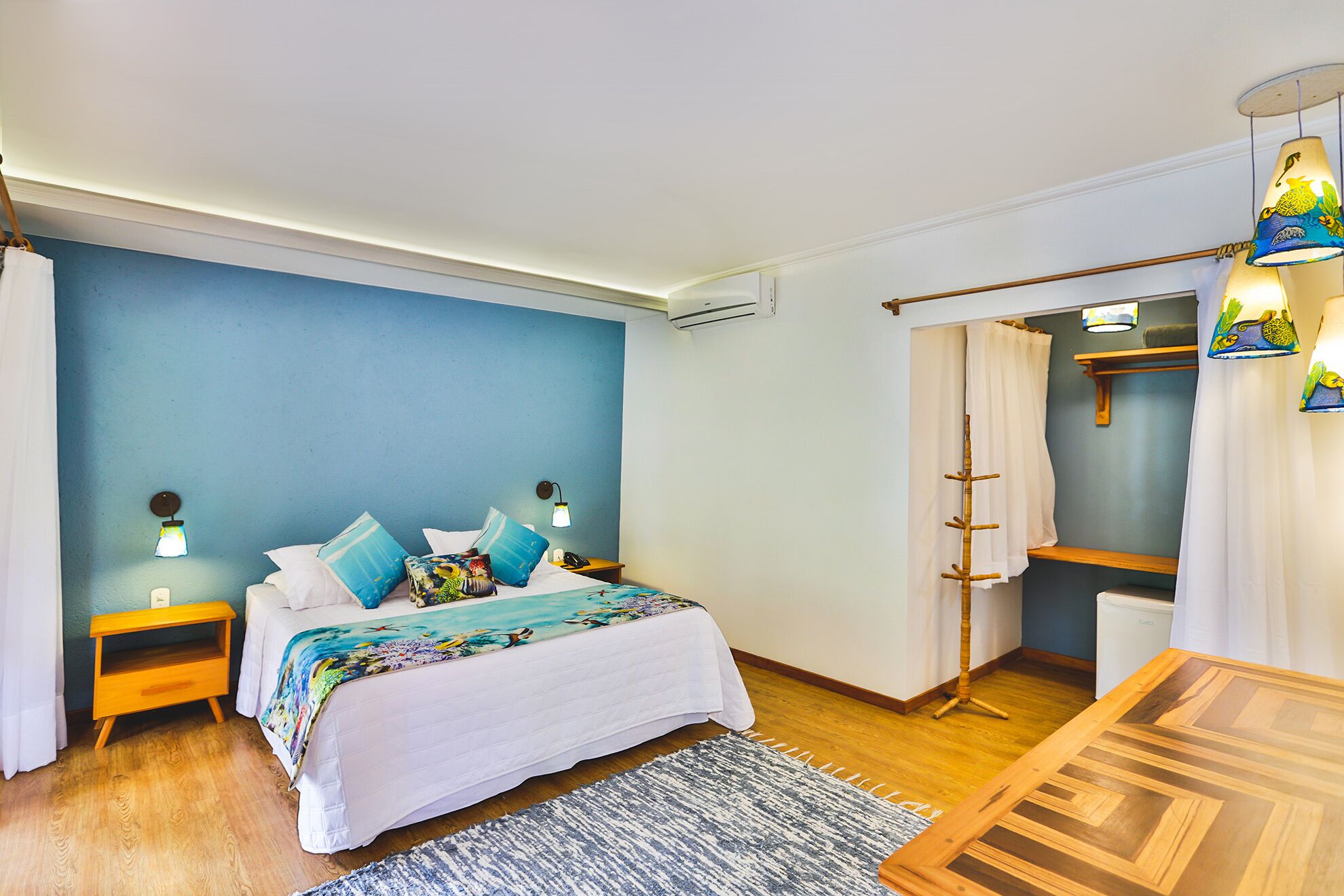 A bedroom with a bed, bedside lamps, a wooden nightstand, a desk, a chair, a wardrobe, and a hanging lamp.