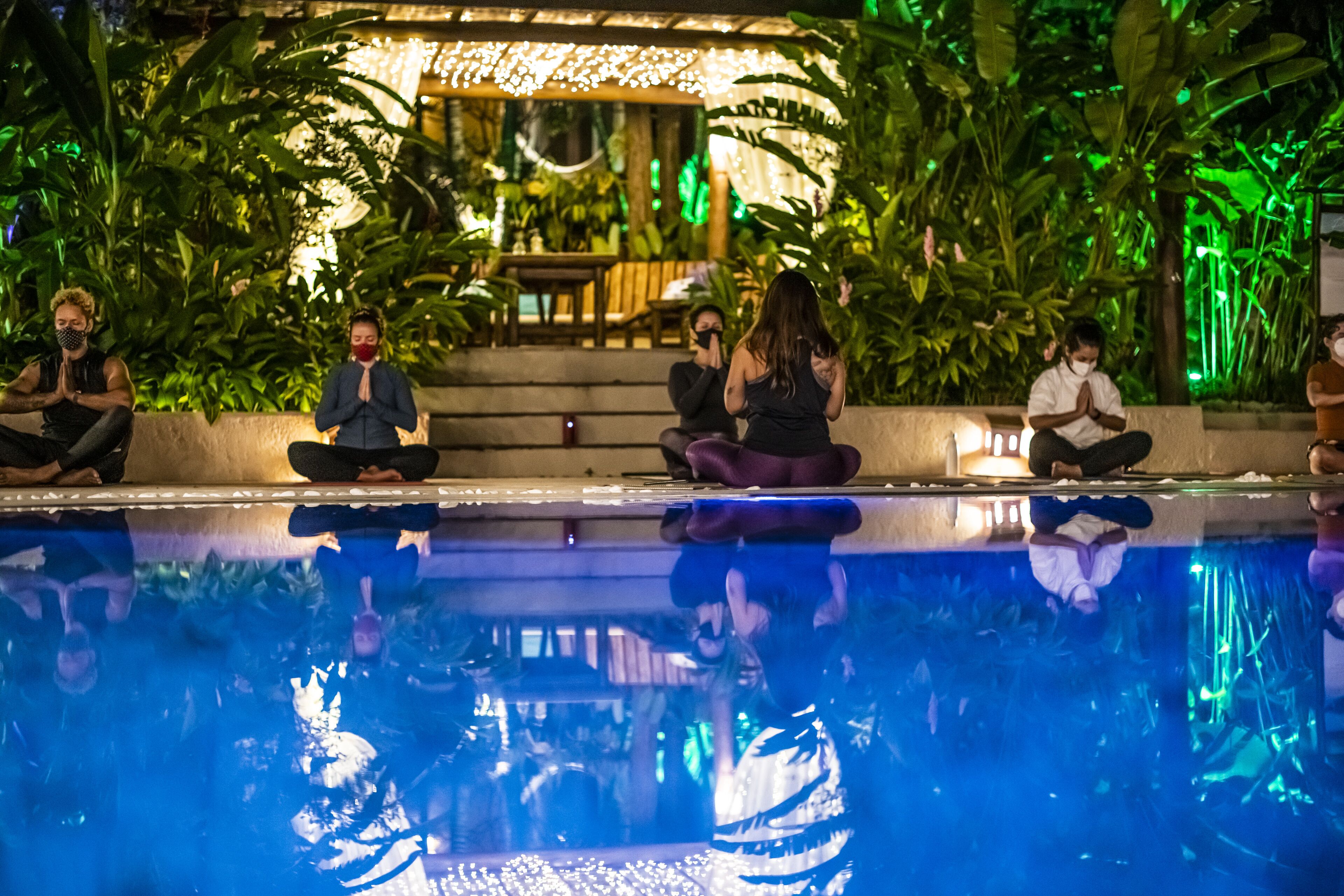 A group of people sitting by a poolside, engaged in a meditative practice.