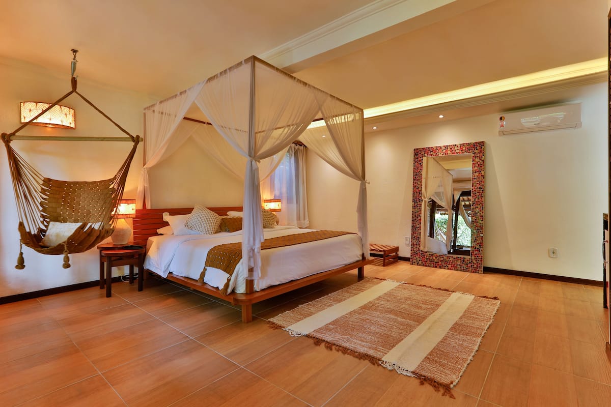 A spacious bedroom with a four-poster bed, a hanging chair, and a large mirror.