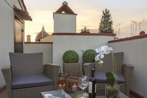 A balcony with wicker furniture, a glass table with a bottle and glass, and potted plants. - Archino di San Piero (Florence)
