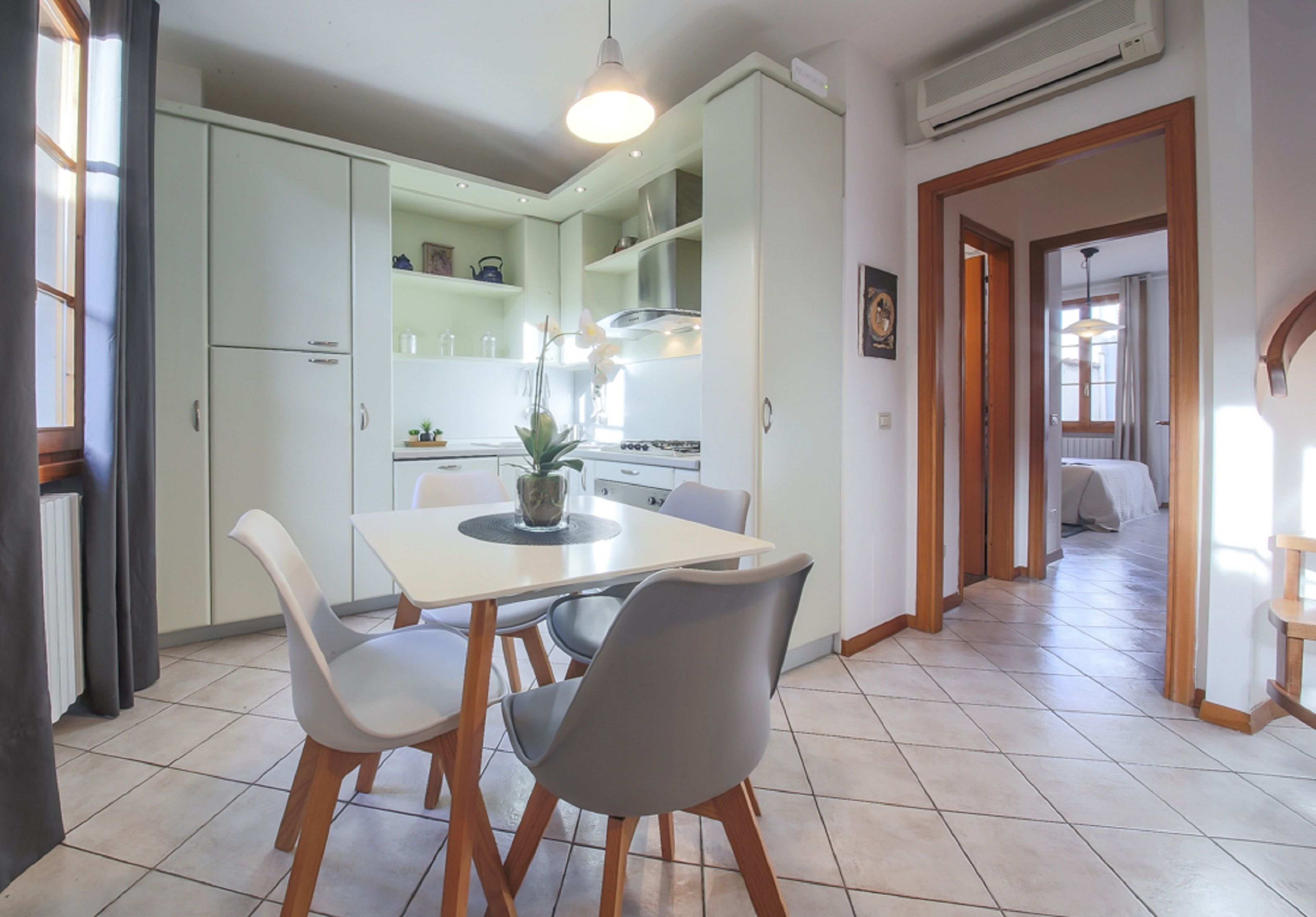 A modern kitchen with white cabinets, a dining table with chairs, and an air conditioning unit on the wall.