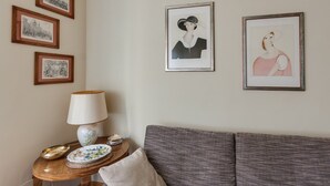 Una sala de estar con un sofá gris, una mesita de madera con una lámpara, y tres cuadros en la pared.