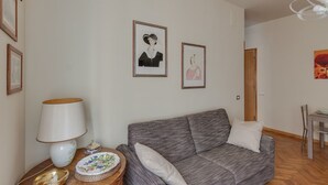 Una sala de estar con un sofá gris, una mesita redonda con una lámpara y dos cuadros enmarcados en la pared.