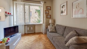 Un salón con sofá, televisor, radiador y ventana con cortinas.