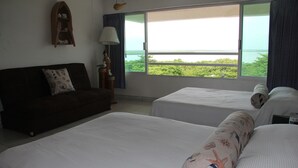 Habitación de hotel con dos camas, un sofá, una lámpara y vista al mar.