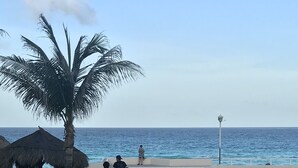 Un sendero pavimentado que conduce a una playa con palmeras, una estructura de techo de paja y un farol.