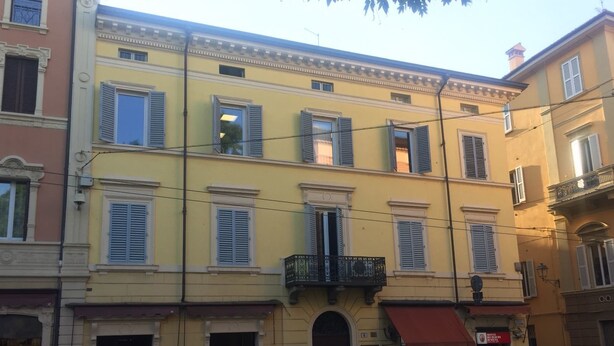 A multi-story building with a yellow facade, multiple windows with shutters, and a ground-floor entrance with a red awning. - BedinBolognaCentro (Bologna)
