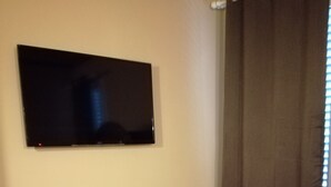 A room with a blue sofa, a flat-screen TV mounted on the wall, and a window with curtains. - BedinBolognaCentro (Bologna)