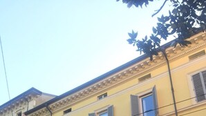 A multi-story building with a yellow facade, multiple windows with shutters, and a red awning. - BedinBolognaCentro (Bologna)