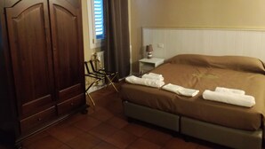 A hotel room with a bed, a wooden wardrobe, a chair, and a nightstand with a lamp. - BedinBolognaCentro (Bologna)