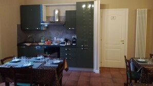 A dining area with a table set for four, a kitchen with dark cabinets, a microwave, and a stove. There is a chandelier above the table and a door with a number on it. - BedinBolognaCentro (Bologna)