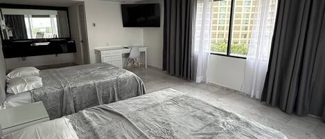 A hotel room with two beds, a desk, a TV, and a window with curtains.
