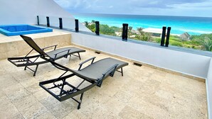 Een balkon met twee loungestoelen en een zwembadje, met uitzicht op een strand met helderblauw water en een tropisch landschap.