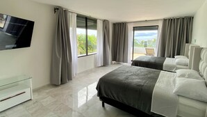Een hotelkamer met twee bedden, een televisie aan de muur en een balkon met uitzicht op zee.