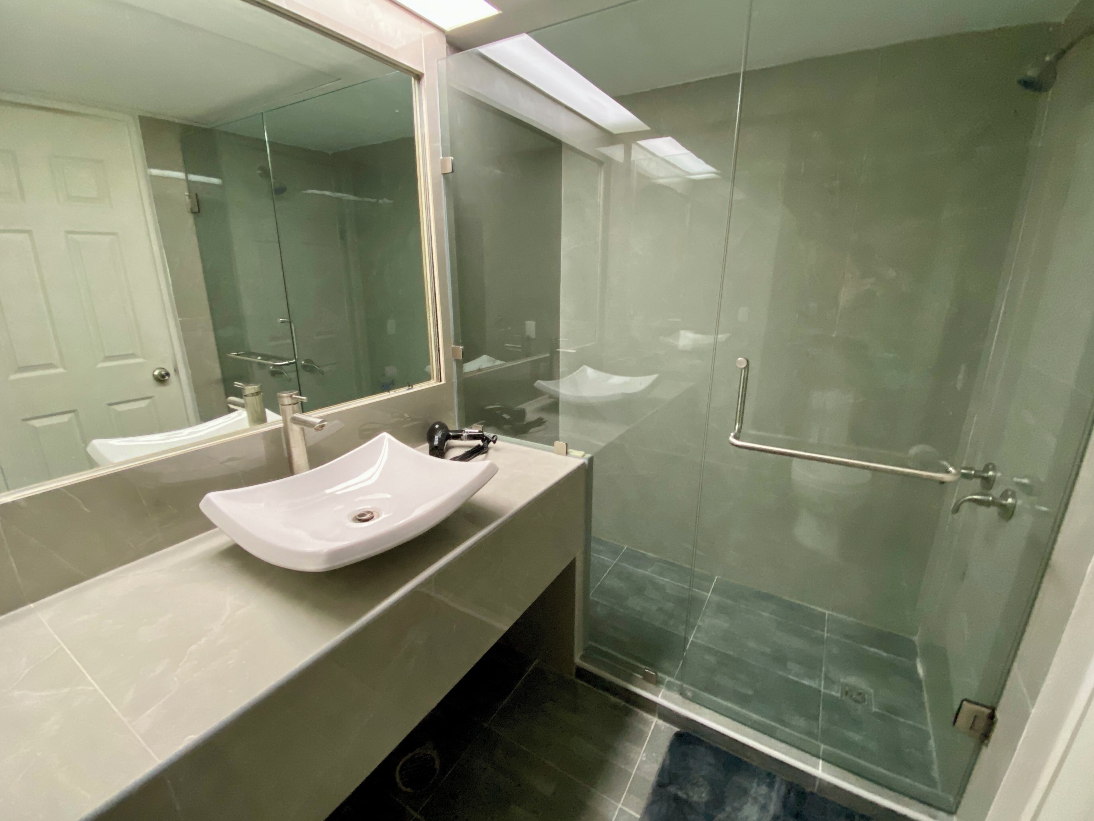 A modern bathroom with a large mirror, a white sink, and a glass shower enclosure.