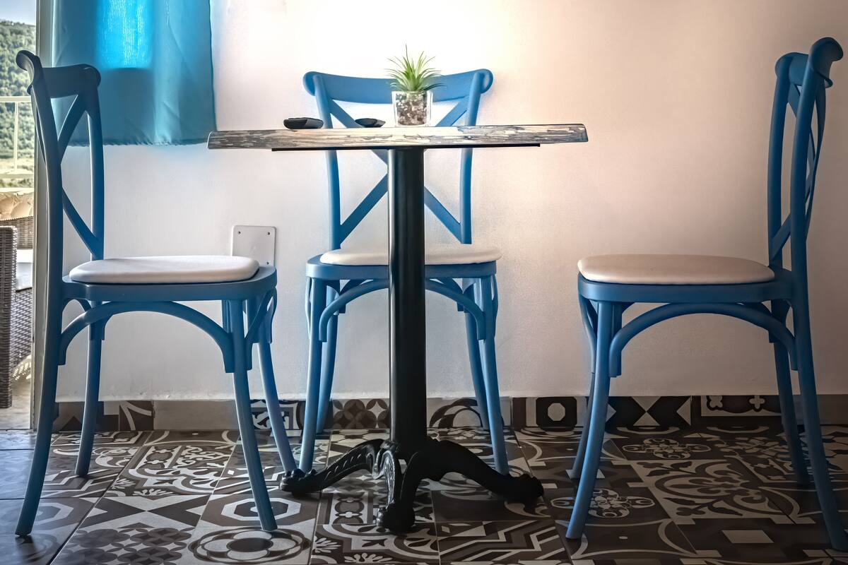 A dining area with a table and chairs, a small plant on the table, and a patterned floor.