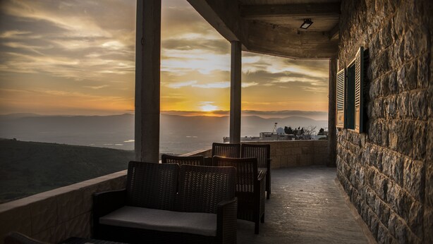 A balcony with wicker furniture overlooking a scenic view of the ocean at sunset. - Old School (Ein Qiniyye)