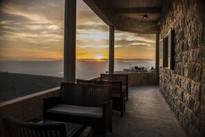 A balcony with wicker furniture overlooking a scenic view of the ocean at sunset. - Old School (Ein Qiniyye)
