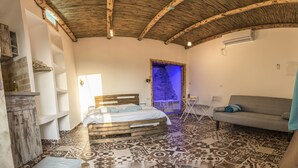 A bedroom with a wooden bed, a grey sofa, a patterned floor, and a rustic ceiling. - Old School (Ein Qiniyye)