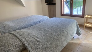 A bedroom with two beds covered in patterned bedding, a television on a wooden stand, and a view of a balcony with a railing. - Beauval Chambre (Seigy)