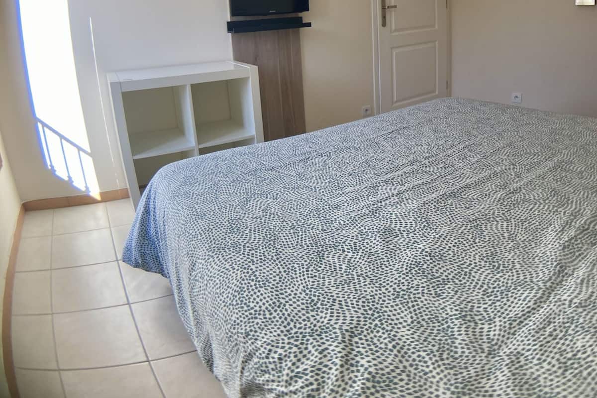 Un dormitorio con cama, televisor montado en la pared, armario y puerta.