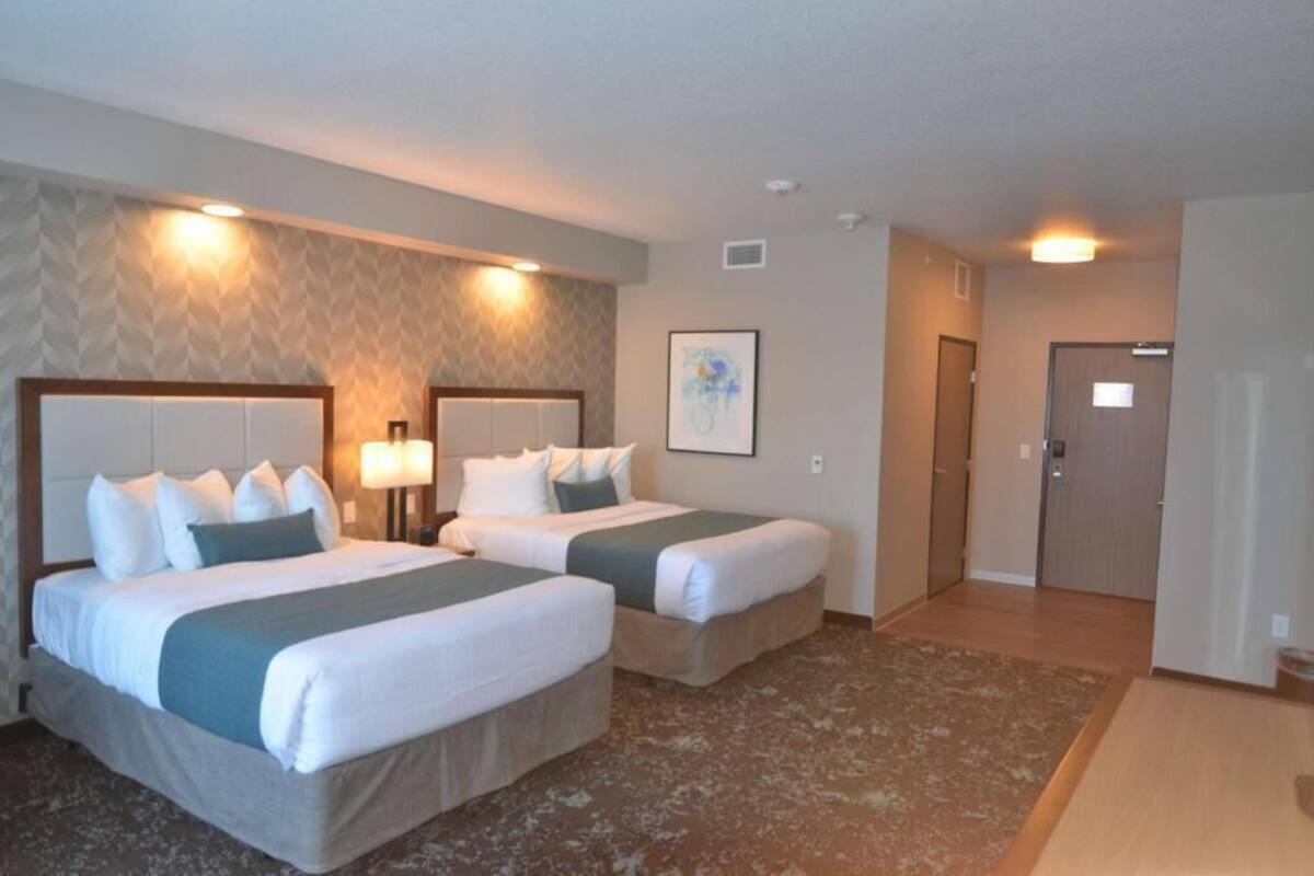 A hotel room with two beds, a large window, and a door leading to a hallway.
