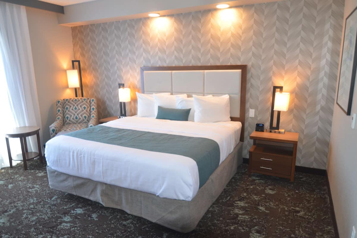 A hotel room with a large bed, two bedside tables, a chair, and a small table.