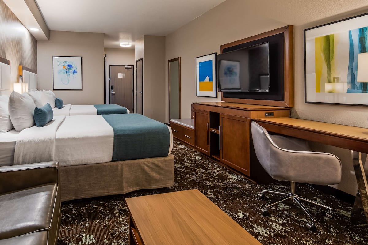 A hotel room with two beds, a desk, a TV, and a seating area.