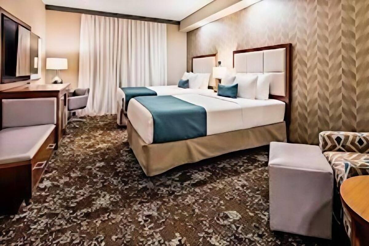 A hotel room with a large bed, two bedside tables, a desk, a chair, and a patterned carpet.