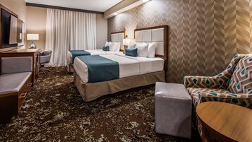 Una habitación de hotel con una cama grande, dos mesitas de noche, un escritorio, una silla y una alfombra estampada.