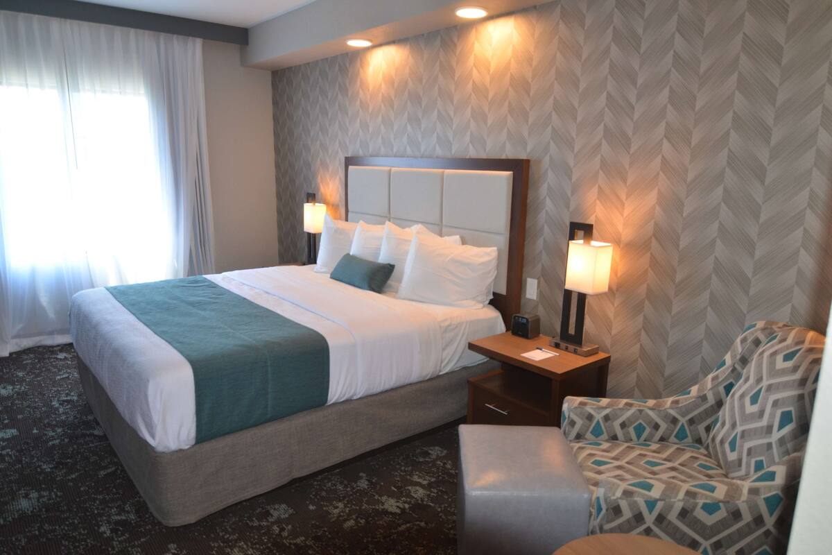 A hotel room with a large bed, two bedside tables with lamps, a patterned wall, and a window with curtains.