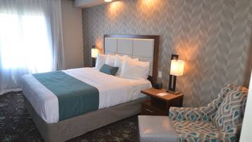 A hotel room with a large bed, two bedside tables with lamps, a patterned wall, and a window with curtains.