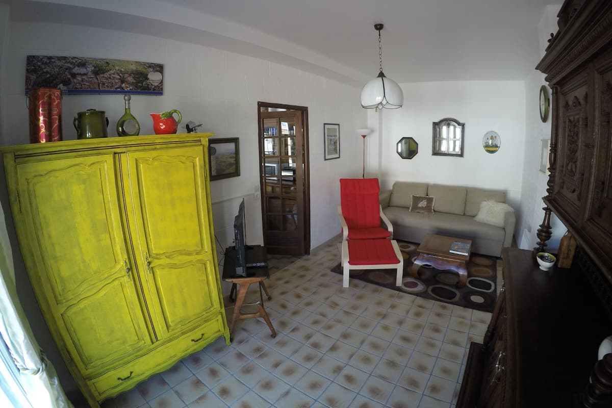 Un salon avec un meuble jaune, un fauteuil rouge, un canapé, un buffet en bois et un sol carrelé.