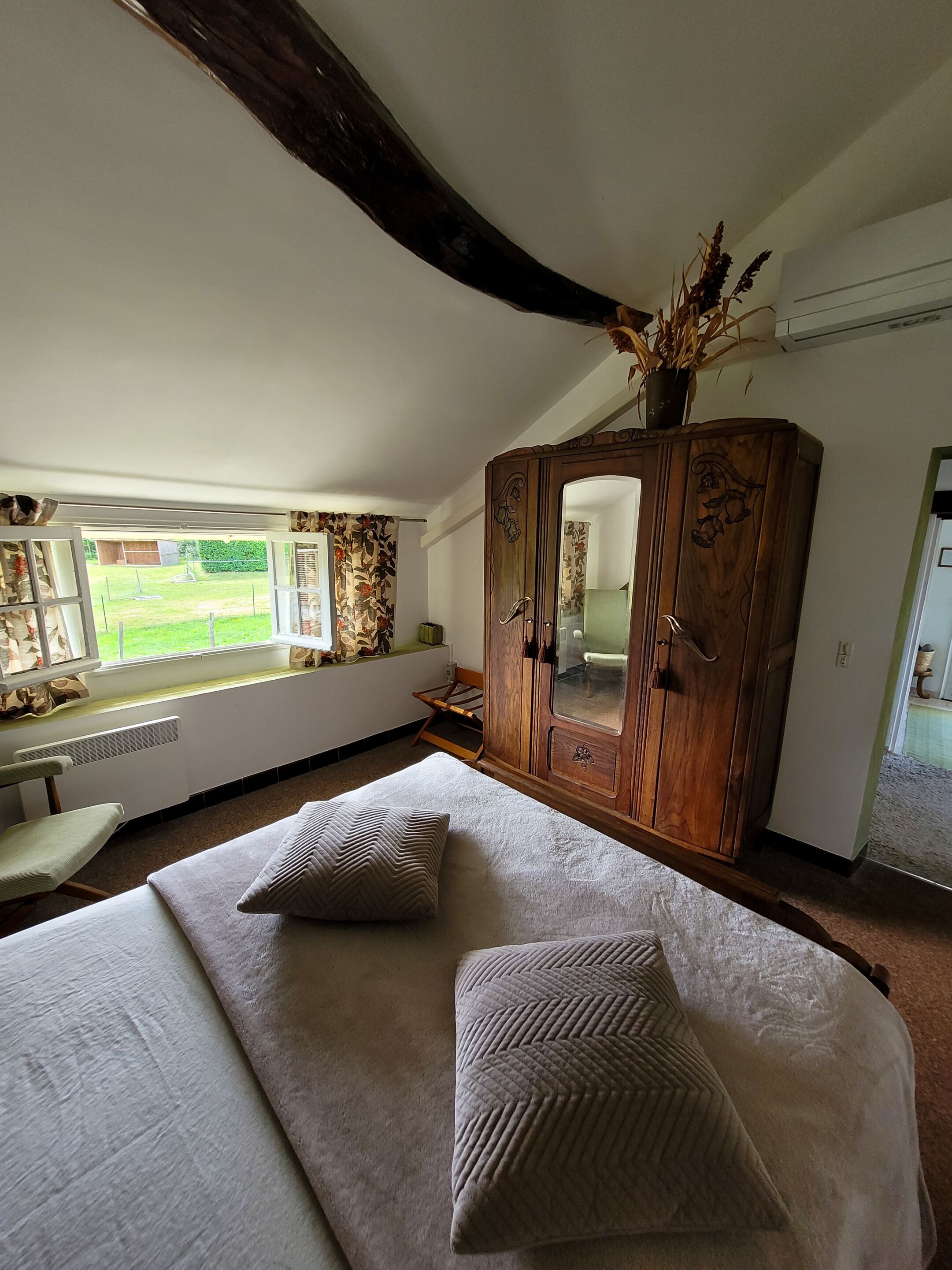 A bedroom with a large bed, a wooden wardrobe, a window with a view of the outdoors, and a radiator under the window.