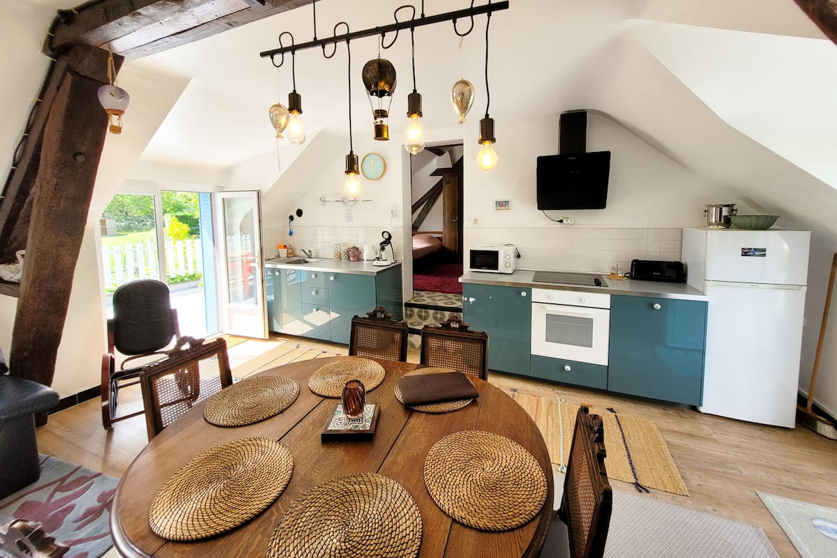 Une cuisine chaleureuse avec une table à manger en bois, des placards bleus et un luminaire suspendu.