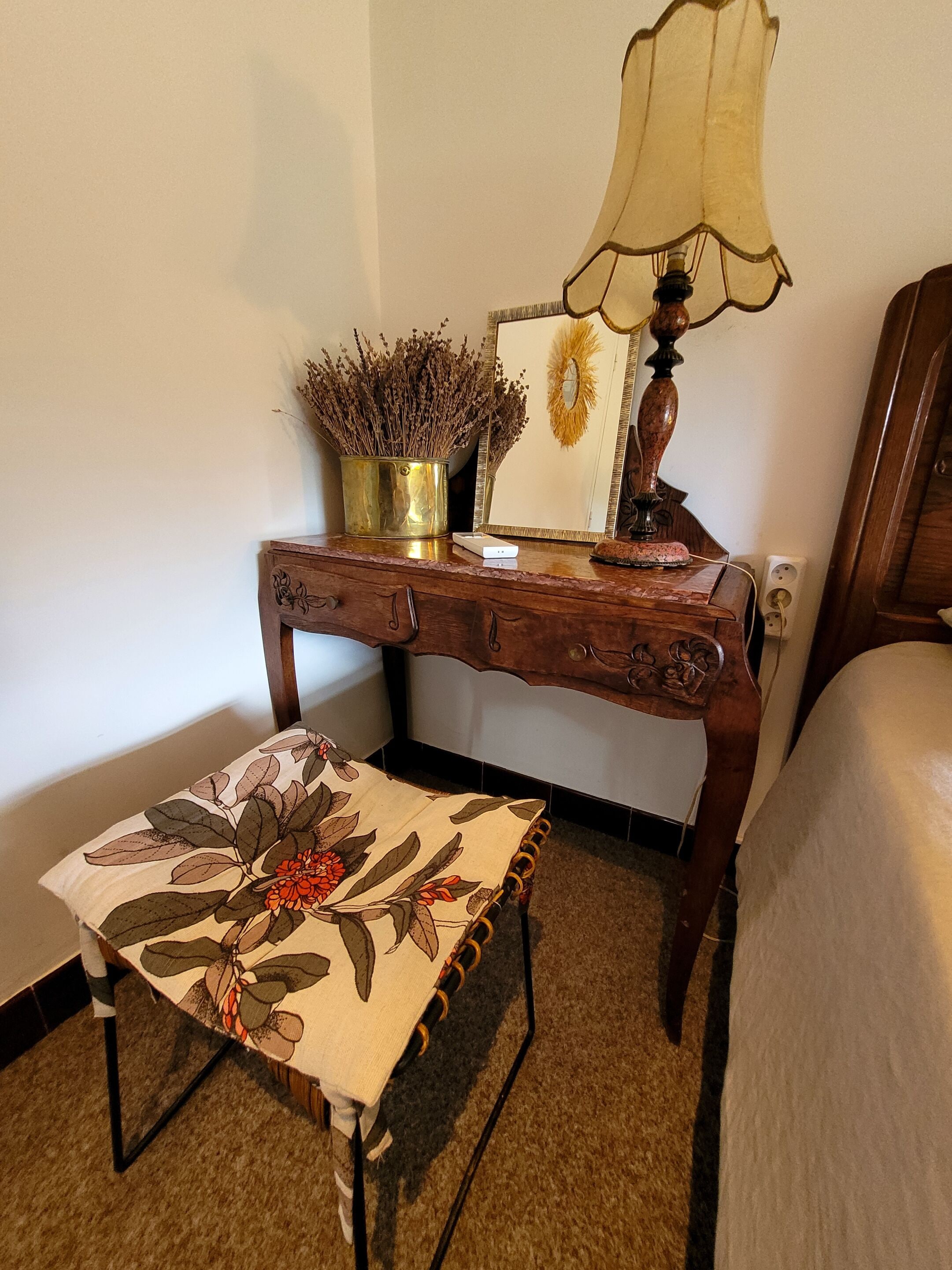 A wooden bedside table with a lamp, a framed picture, and a potted plant.