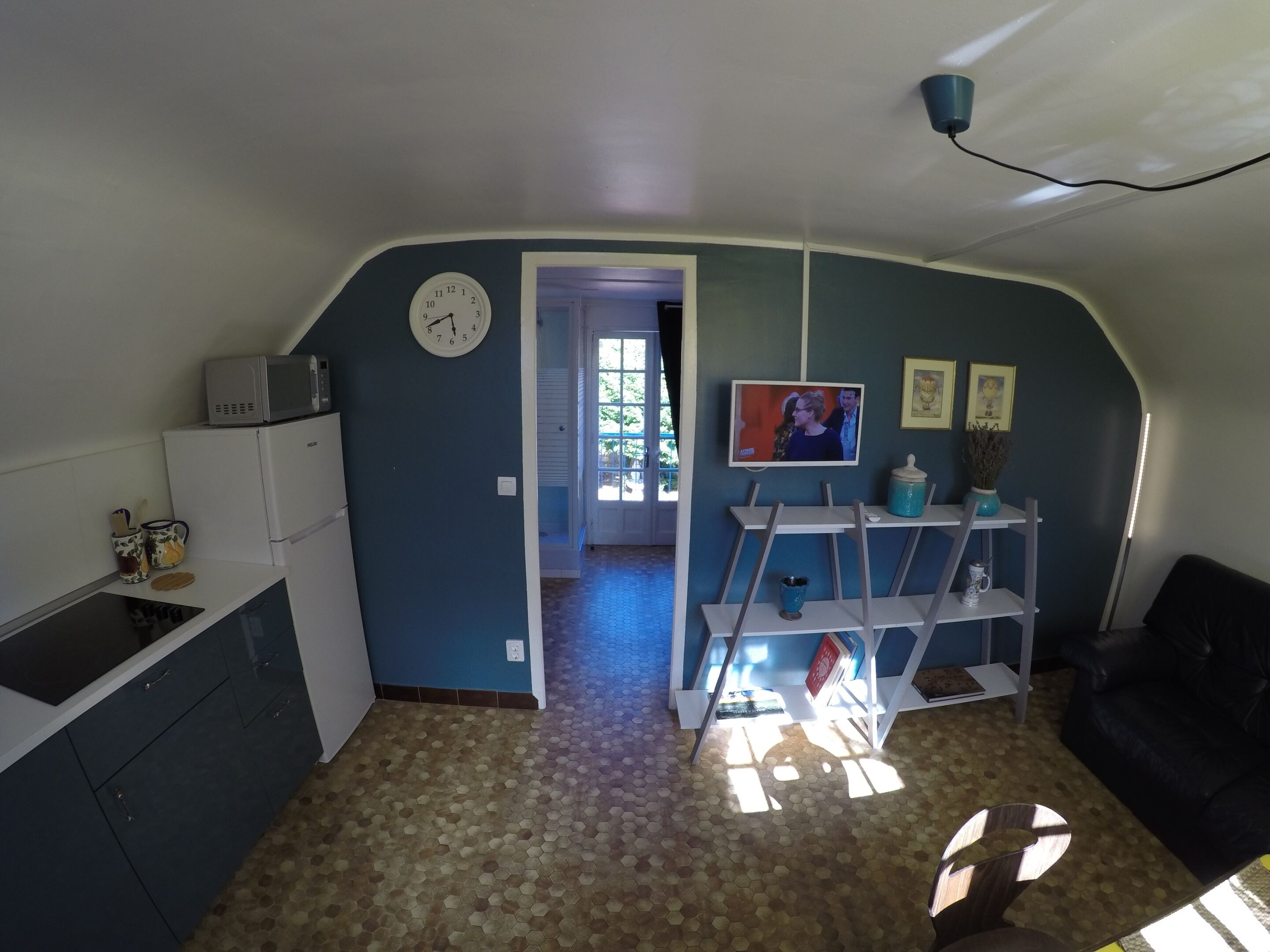 A compact living space with a kitchen area, a dining table with chairs, a sofa, and a television.