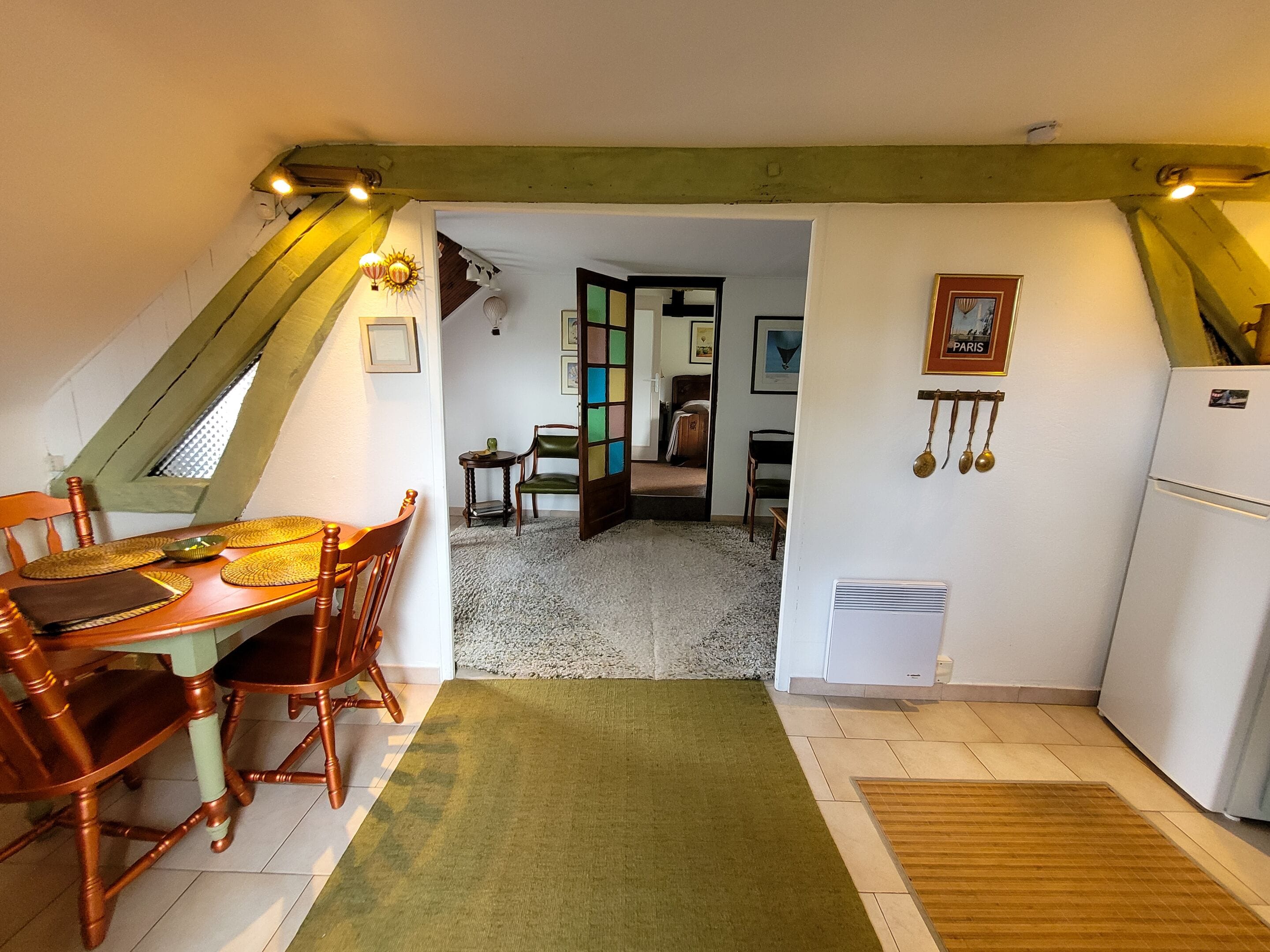 A cozy kitchen with a dining area, a green rug, and a view into the living room.