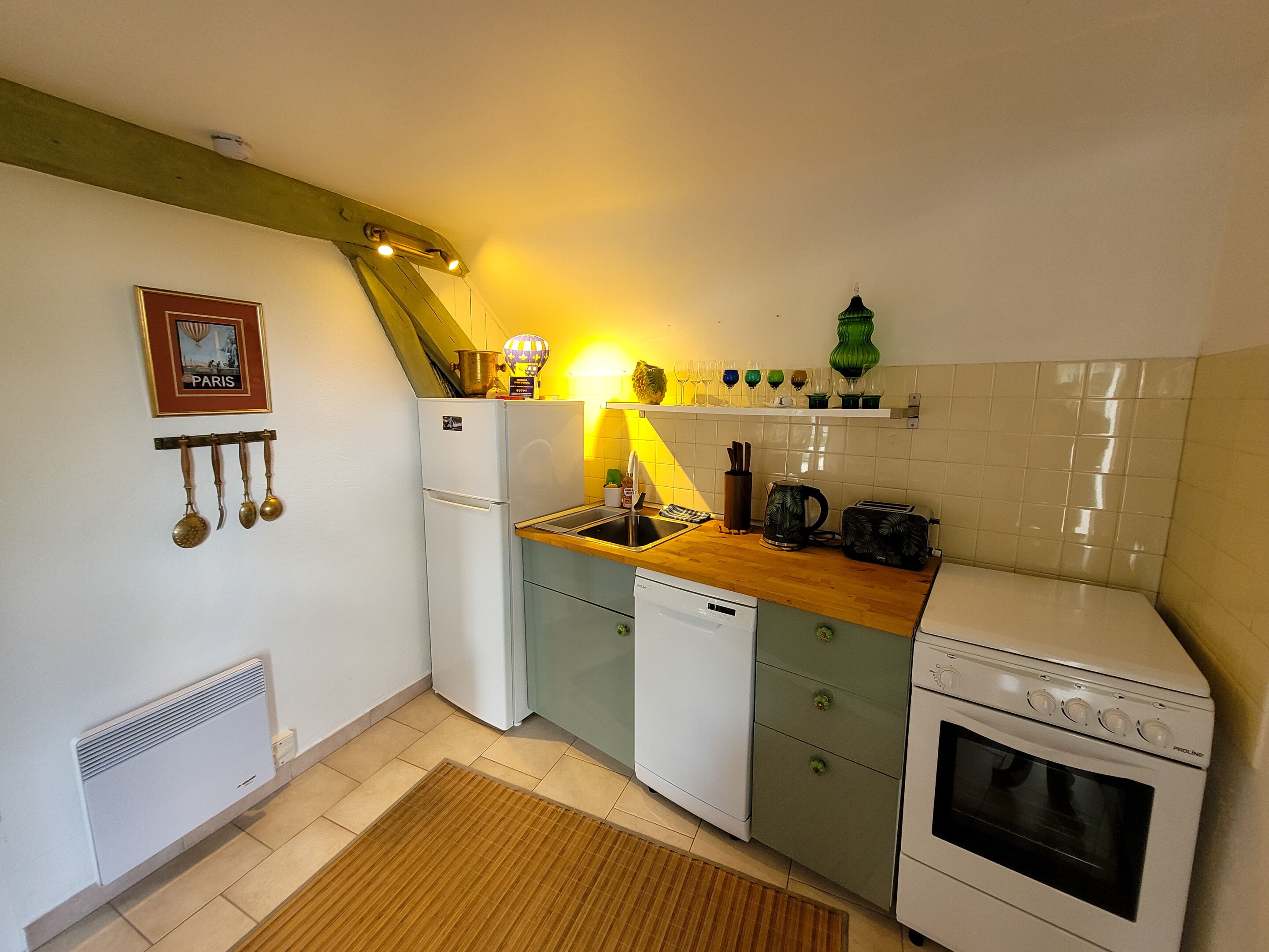 A compact kitchen with a white refrigerator, a stove, and a sink. There is a wooden countertop, a green vase, and a framed picture on the wall.