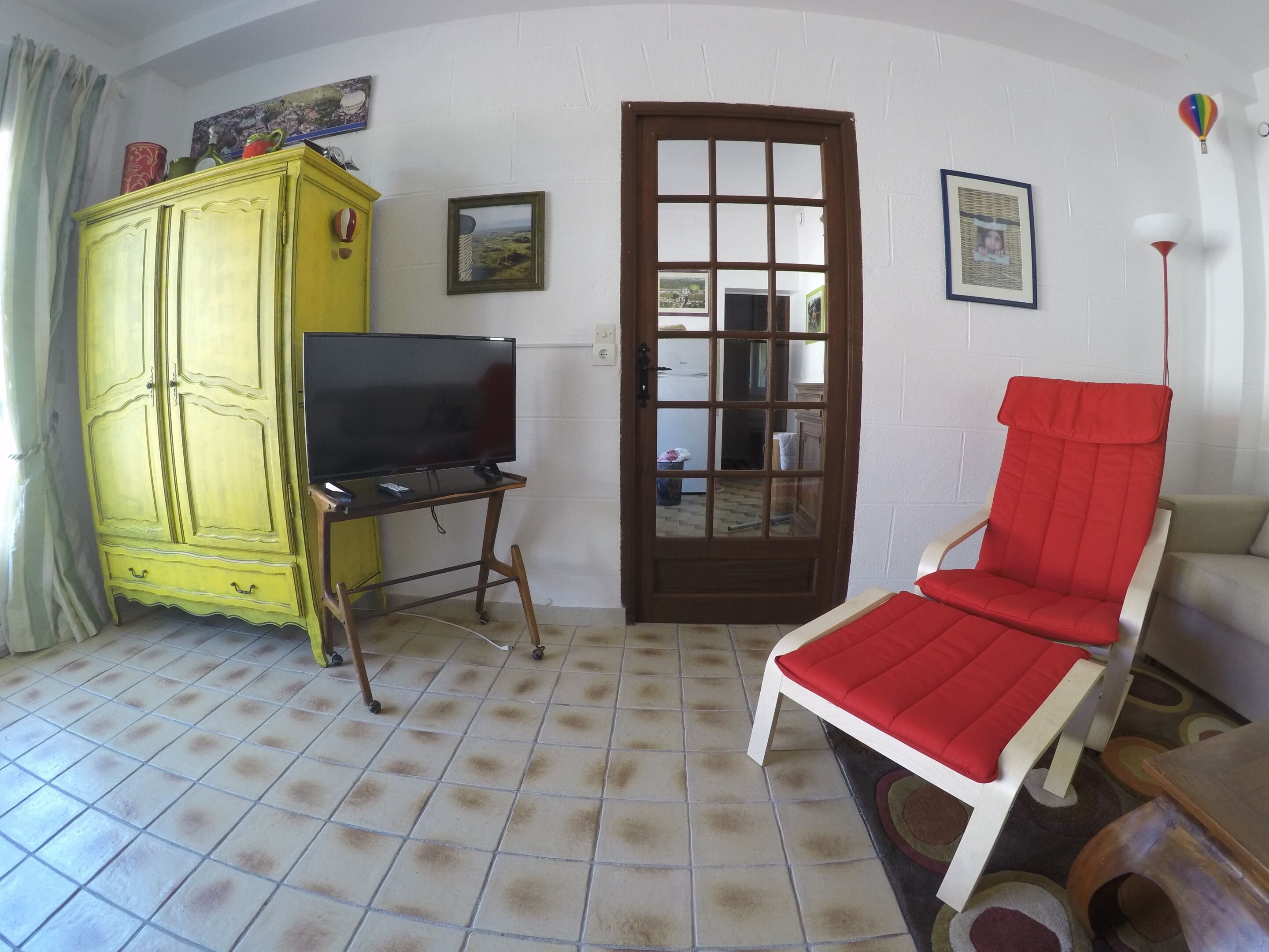 A room with a yellow cabinet, a television on a wooden stand, a red chair, and a door with a glass panel.