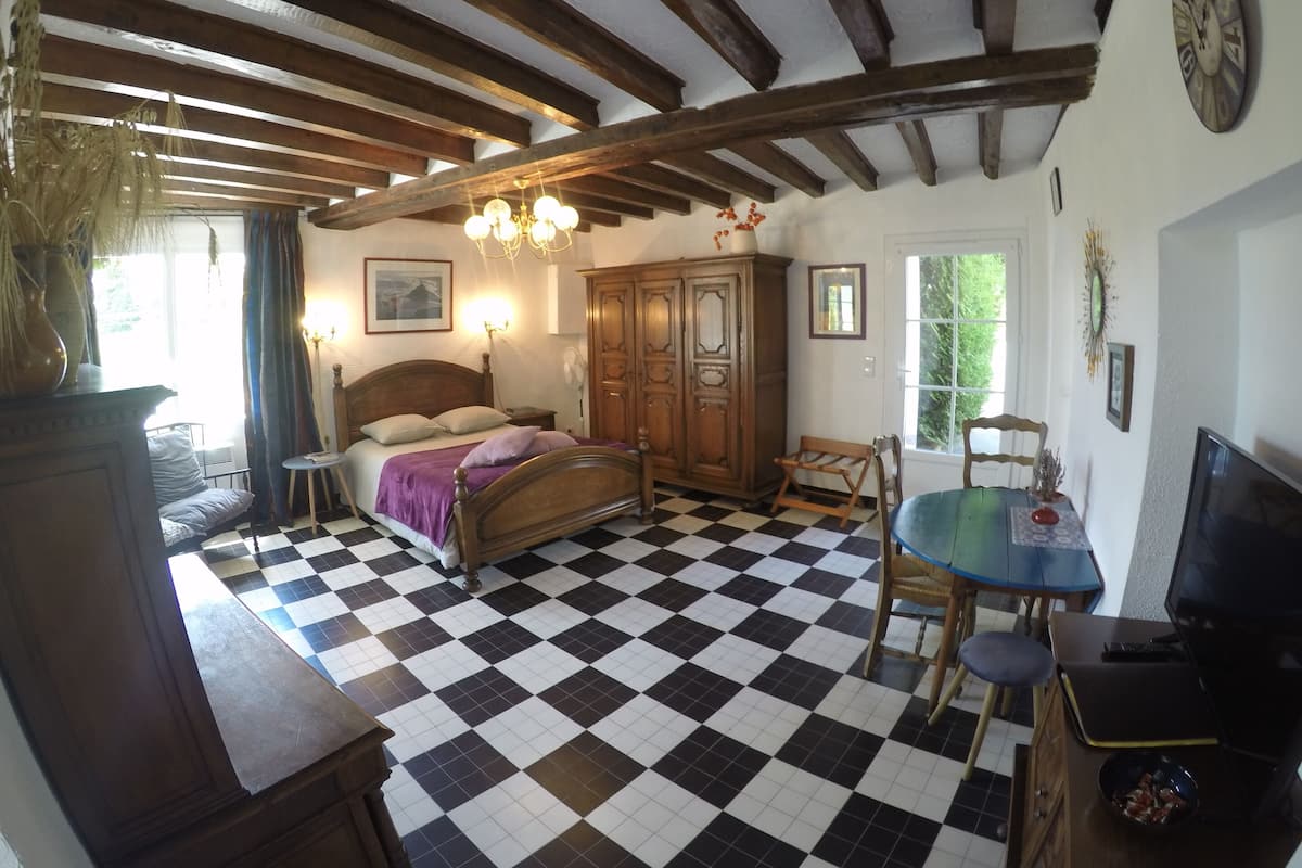 Une chambre avec un sol à carreaux, un lit en bois, une armoire et un téléviseur.