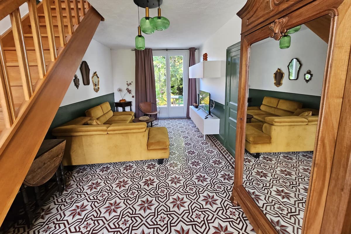Une pièce avec un sol à motifs, un canapé, un miroir et un escalier.