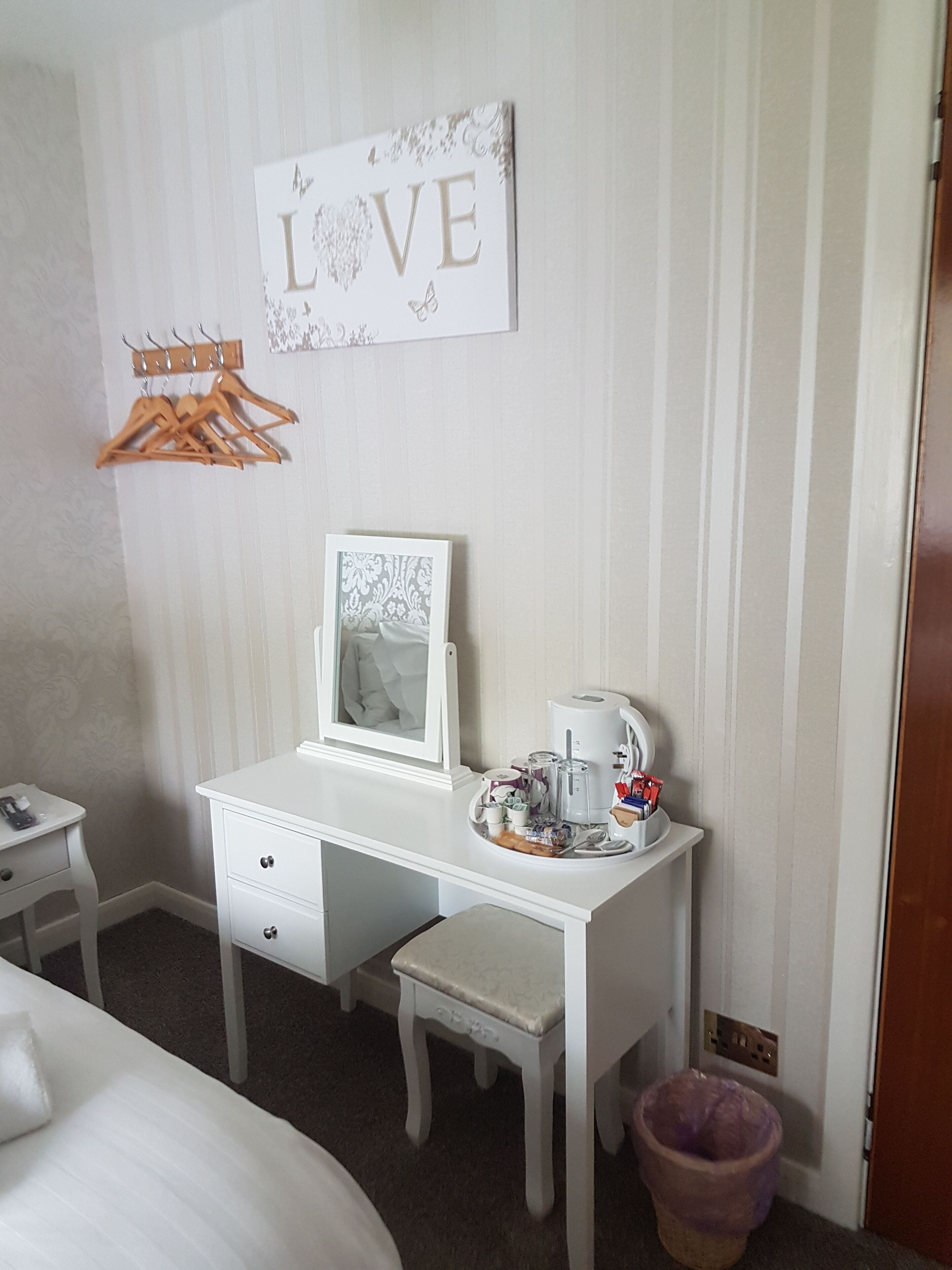 A neatly arranged bedroom with a white dresser, a small bedside table, a hanging coat rack, and a wall-mounted picture frame.