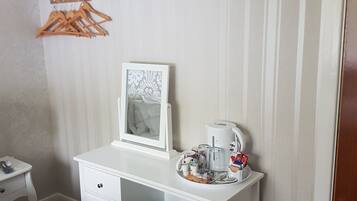 Une chambre à coucher bien rangée, avec une commode blanche, une petite table de chevet, un porte-manteau mural et un cadre photo fixé au mur.