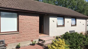 A two-story house with a brick facade, a tiled roof, and a small front yard with a bench and potted plants. - Foinaven Bed & Breakfast (Ullapool)
