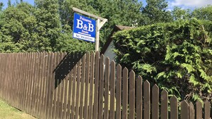 A blue sign with white text stating "Foinaven B&B No Vacancies" against a backdrop of a wooden fence and lush greenery. - Foinaven Bed & Breakfast (Ullapool)