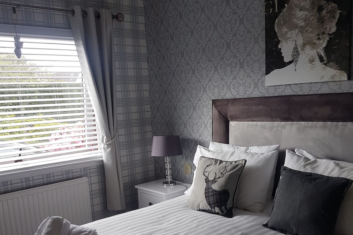 A neatly made bed with rolled towels, a bedside lamp, and a patterned wall.