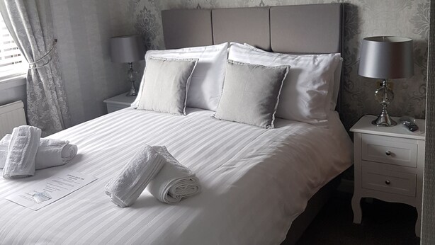 A neatly made bed with pillows, a bedside table with a lamp, and a painting on the wall. - Foinaven Bed & Breakfast (Ullapool)